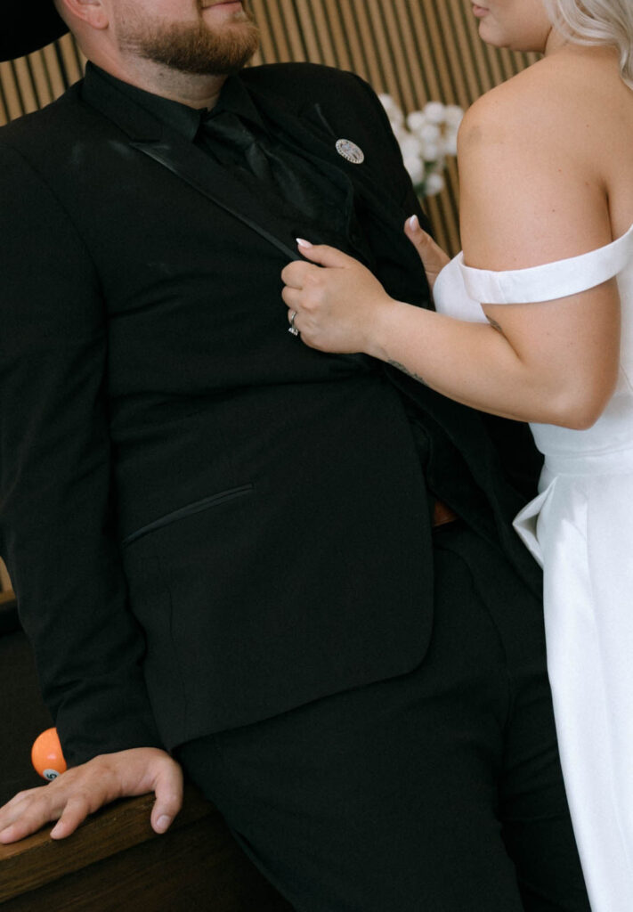 Bride gripping the groom’s lapel while he leans against a pool table, wearing a black cowboy hat at White Barn Weddings in Emmett, Idaho
