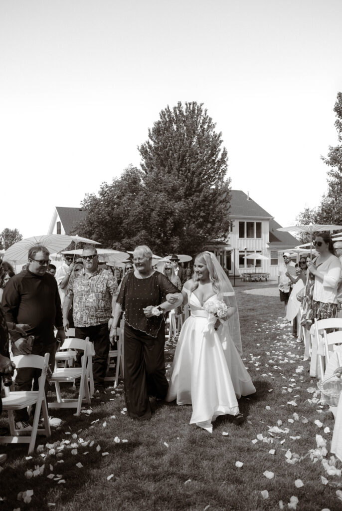 Bride McKenzie walking down the aisle in a satin gown with a sweetheart neckline, escorted by her grandma
