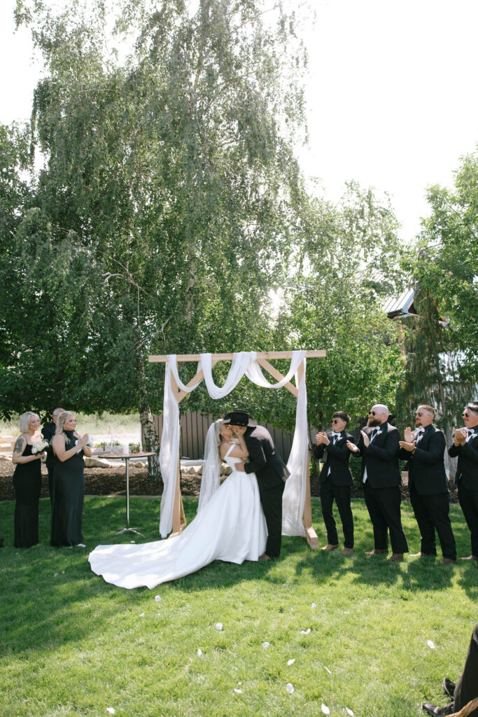 Bride and groom sharing their first kiss under a draped wooden arch during their Idaho barn wedding