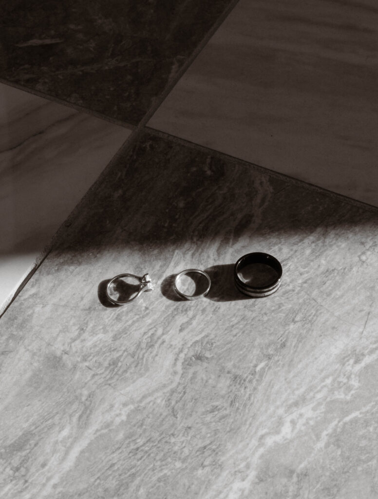 Close-up of McKenzie and Conner’s wedding rings, engagement ring, bride’s band, and groom’s band, displayed on marble tile in natural light