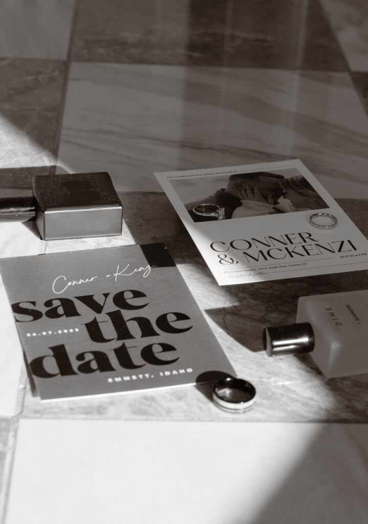 Flat lay of McKenzie and Conner’s wedding save-the-date card and invitation suite with engagement rings, perfume, and groom’s cologne, styled on marble tile, photographed by Krysta Timmons Photography