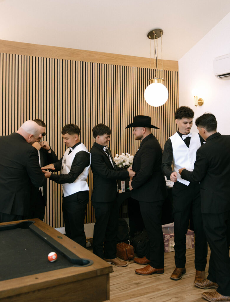 Groomsmen helping each other with ties and jackets in the stylish groom’s suite at White Barn Weddings in Emmett, Idaho, photographed by Krysta Timmons Photography