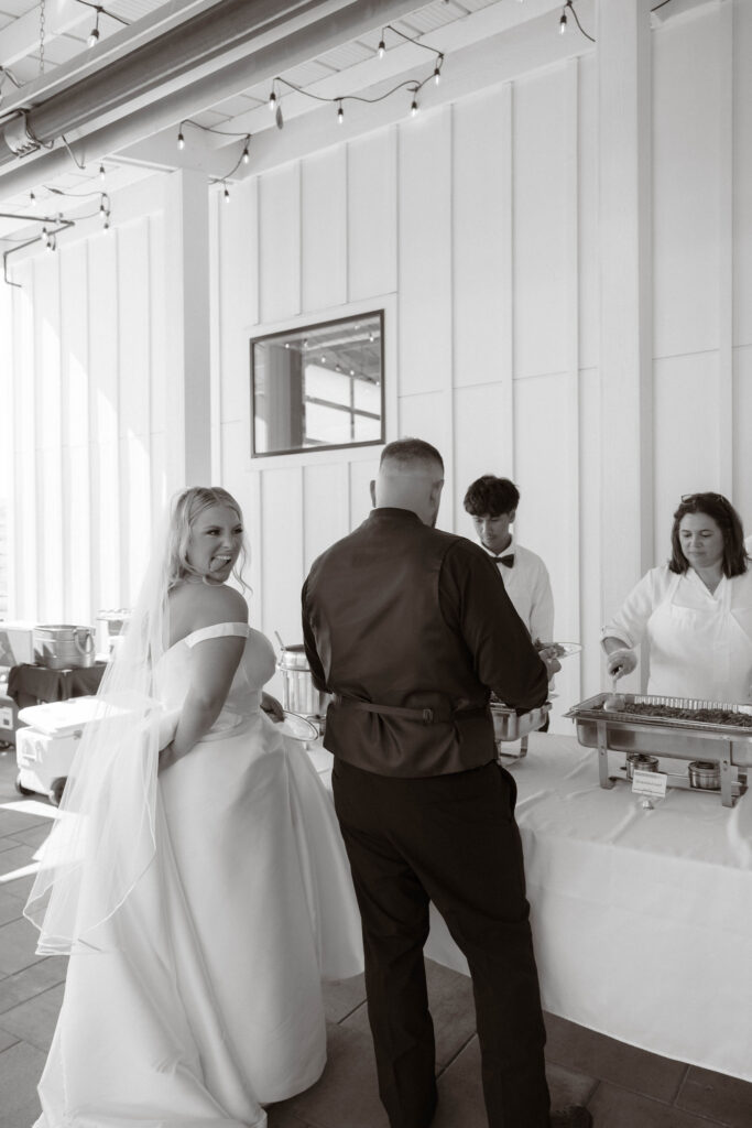 Bride McKenzie and groom Conner smiling as they go through the buffet line, served by Casablanca Cuban Grill at their White Barn Weddings in Emmett Idaho