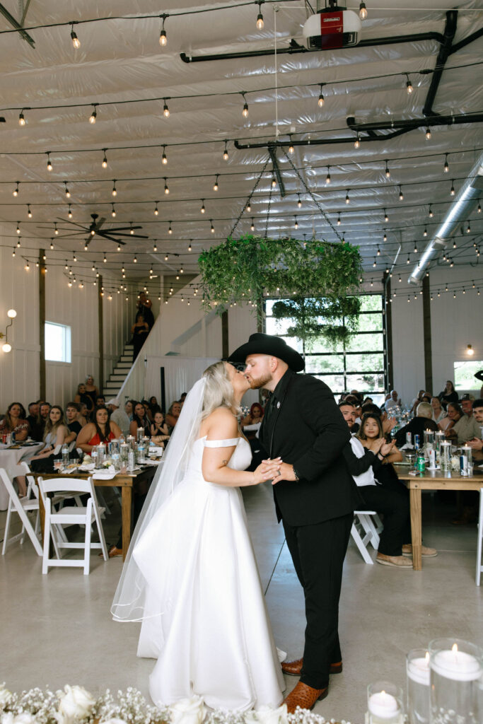 Bride McKenzie and groom Conner sharing their first dance kiss under a hanging greenery chandelier at White Barn Weddings in Emmett Idaho